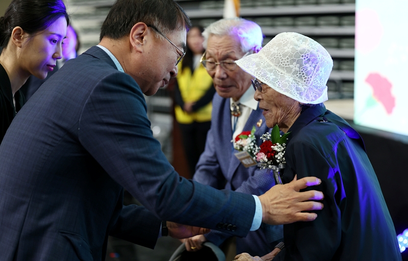 كيم سانغ-هان نائب عمدة إدارة سيئول (على اليسار) يقدم باقة زهور القرنفل إلى السيد بارك تيه-نام (96 عاما) والسيدة كيم أوك-ريه (93 عاما) في الحفل التذكاري للذكرى الثانية والخمسين ليوم الوالدين الذي أقيم يوم 8 مايو في استاد جانغتشيونغ الرياضي بحي جونغ غو في سيئول.