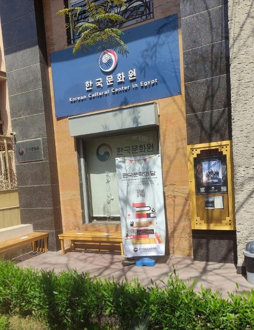 تظهر الصورة لوحة إعلان فعالية شهر الأدب الكوري الموجودة خارج مبنى المركز الثقافي الكوري بمصر.