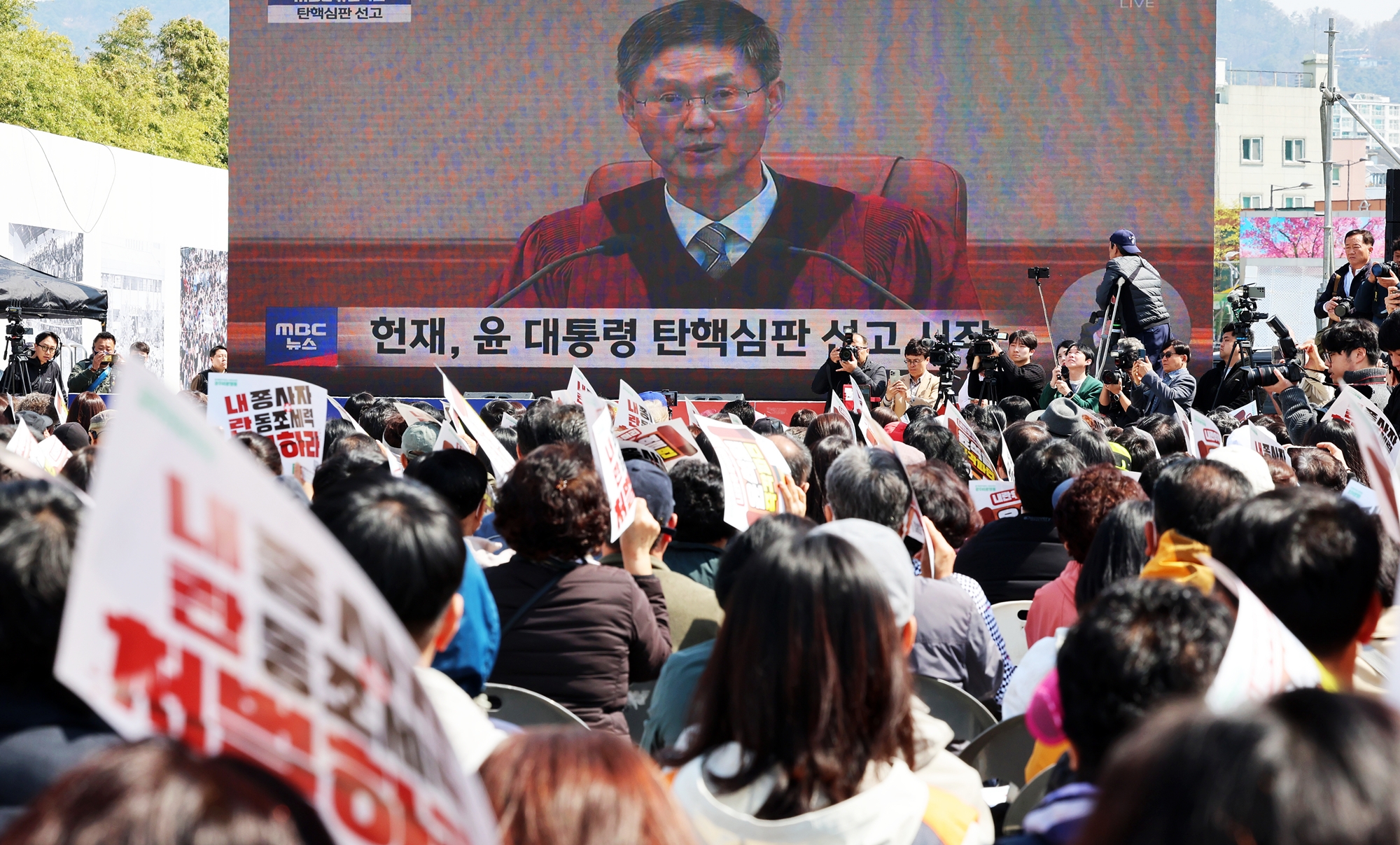 قضت المحكمة الدستورية، في جلسة النطق بالحكم في قضية عزل الرئيس يون سوك-يول في 4 أبريل، بالإجماع من قبل جميع أعضاء المحكمة الثمانية، وقبلت قرار الجمعية الوطنية بعزله. وبدأ سريان مفعول العزل فورًا، ومن ثم فقد الرئيس السابق يون منصبه كرئيس للجمهورية اعتبارًا من تلك اللحظة. ويأتي هذا بعد 122 يومًا من إعلان حالة الطوارئ في 3 ديسمبر من العام الماضي، و111 يومًا من تقديم عريضة العزل في 14 من نفس الشهر. تُظهر الصورة أحد المواطنين وهو يتابع البث المباشر لحكم المحكمة الدستورية في قضية عزل الرئيس يون سوك-يول، صباح يوم 4 أبريل في ساحة 18&middot;5 الديمقراطية بمنطقة دونغ-غو في مدينة غوانغجو. (الصورة من وكالة يونهاب للأنباء(