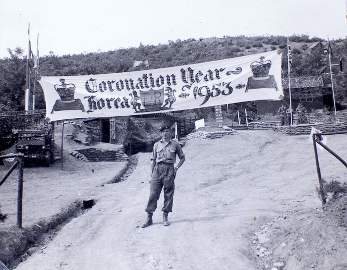 Signals Officer Gunner Doug Leyland poses under his painted banner in 1953. The banner says, 