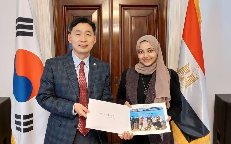 المراسلة الفخرية آلاء عاطف مع الوزير المفوض والقنصل العام ’تشوي بيونغ-سون‘ لسفارة جمهورية كوريا بالقاهرة أثناءاستلام الصورة التذكارية المبعوثة من المكتب الرئاسي ومقره سابقا البيت الأزرق في مارس 2022 (الصورة من آلاء عاطف)