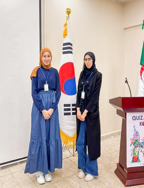 (تظهر الصورة المراسلتين الفخريتين عنان شيماء وبوحنيكة إيمان أمام العلم الكوري (الصورة من المراسلة الفخرية بوحنيكة إيمان