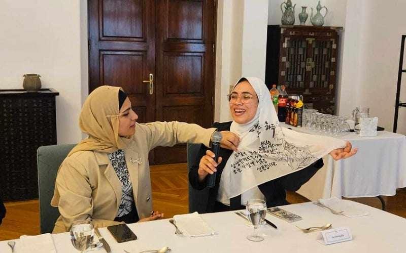 إيمان تقدم عملها الفني لسيادة السفير الكوري كيم يونج هيون وتشرح ما قامت بكتابتة الصورة منها مع الأذن.
