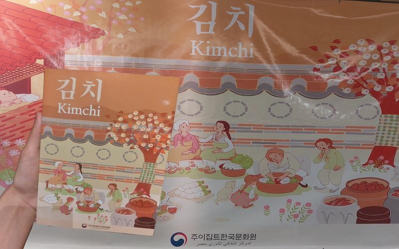 الصورة توضح كتيب الكيمتشي مع بوستر الفعالية (الصورة من خلود خالد ابواليزيد)