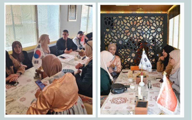 يظهر تصميم الصورة بلواز زينب وهى ترتدي الهانبوك على الطاولة الخاصة باللغة الكورية التي قامت بتنظيمها في ملتقى الفرارة للتبادل اللغوي بمدينة الجلفة بالجزائر (الصور من بلواز زينب وتم اخذ الأذن منها لاستخدامها في المقال)
