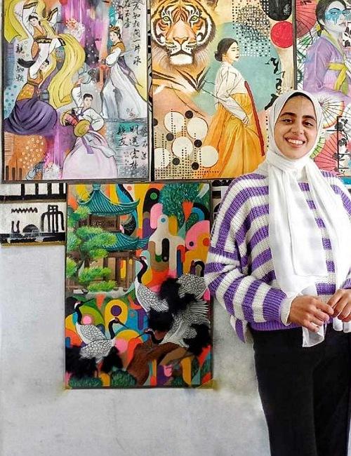 تظهر الصورة نغم مجدي مع اللوحات التي قامت برسمها (الصورة من نغم مجدي وتم اخذ الأذن منها لاستخدامها في المقال)