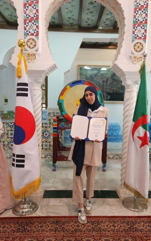 المراسلة الفخرية عنان شيماء حاملة لشهادة التعيين كداعمة رقمية داخل السفارة الكورية في الجزائر. (الصورة من عنان شيماء)