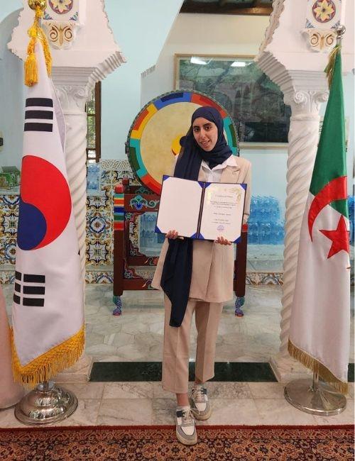 المراسلة الفخرية عنان شيماء حاملة لشهادة التعيين كداعمة رقمية داخل السفارة الكورية في الجزائر.