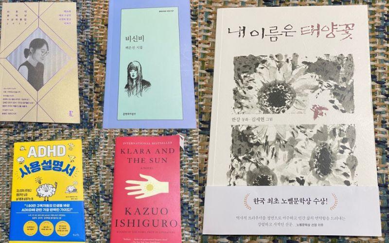 صورة مجمعة للكتب التي حصلت عليها، على اليمين غلاف كتاب 'اسمي هو زهرة الشمس' لهان كانغ، في الأعلى بجانبها غلاف ديوان 'اللا غامض' لبايك أون سون، بجانبه في أقصى الصورة غلاف المجموعة القصصية 'حكايات التفاحة ورينغو'، في الأسفل على اليمين غلاف رواية 'كلارا والشمس' لكازو إيشيغورو، وعلى اليسار غلاف كتاب 'كيف تتعامل مع اضطراب تشتت الإنتباه وفرط الحركة' لجيسيكا مكابي (الصور من إيمان الأشقر.)