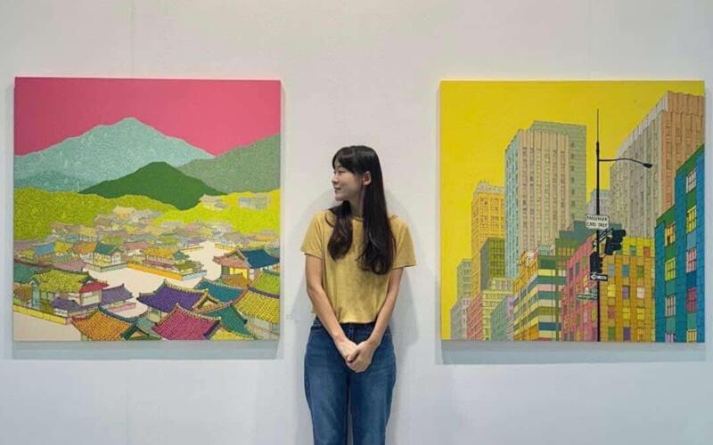 نرى في الصورة الفنانة الكورية ييريم لي بجانب لوحاتها في معرض كيياف 2025 في كوريا (الصور من ييريم لي وتم أخذ الإذن لاستخدامها.)