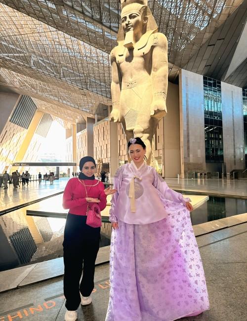 الصورة تجمع المصممة ناريمان طلال والكاتبة الكورية بيونغ ليم-جي في المتحف المصري الكبير مع التصميم الذي صممته خصيصًا لها؛ تصميم هانبوك ملكي باللون البنفسجي مطرز بخيوط الحرير الذهبية والطباعة الذهبية على التنورة على شكل فراشات. (الصورة من ناريمان طلال مع الإذن)