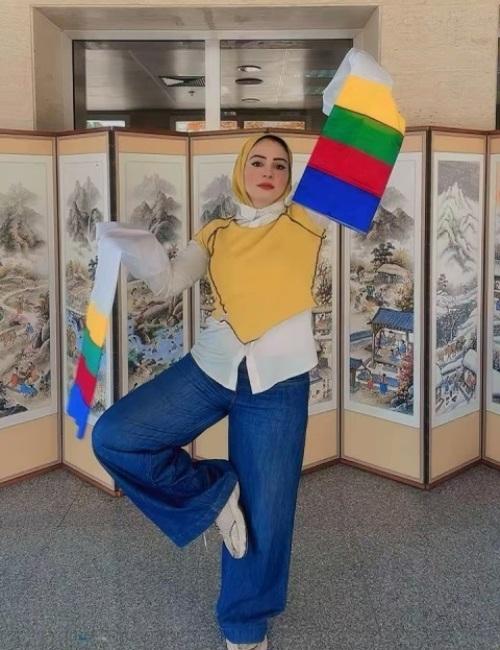الصورة تظهر لقطة استعراضية مبهجة لرحاب رمضان وهي تؤدي رقصة كورية تقليدية بالمراوح الملونة أمام ساتر كوري تراثي يعرف باسم بيونغ بونغ مزين برسومات الطبيعة والزهور. (مصدر: رحاب رمضان)