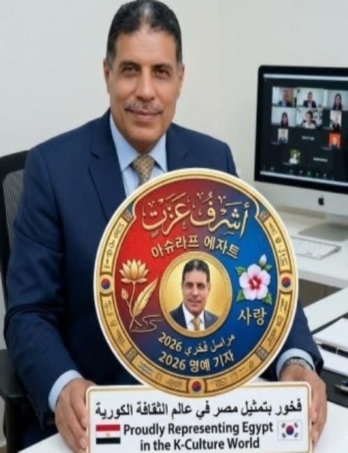 المراسل الفخري المصري أشرف عزت مبتسماً وهو يحمل درعاً تذكارية دائرية ومزخرفة تحتفي باختياره لعام 2026، ويظهر في أسفلها شعار 