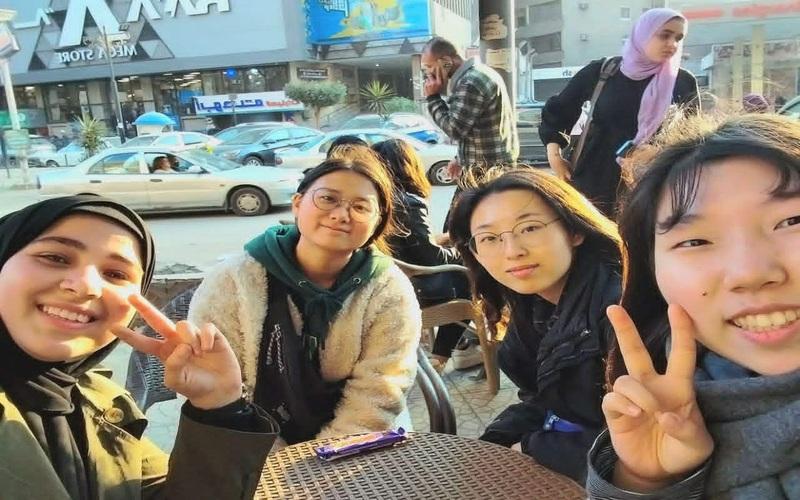 تجمع شبابي يضم شروق أيمن مع مجموعة من الفتيات يمارسن المحادثة الكورية ويلتقطن لقطة جماعية عفوية في مقهى خارجي وتظهر السيارات في الخلفية. (المصدر: شروق أيمن)