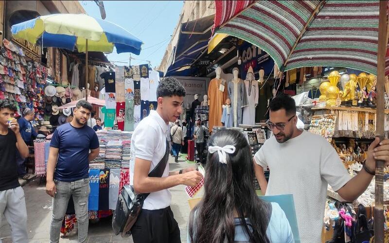 عضو الفريق أحمد برفقة المشرفة على الحملة في أحد المحلات السياحية بخان الخليلي، يعرّفان أحد البائعين باللغة الكورية. (تصوير: أحمد كامل، بعد الحصول على إذن الفريق بالنشر)